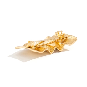 Detail of liquid metal hair clip showing irregular wave texture and polished gold finish