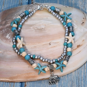 Detail of layered boho anklet with turquoise beads and silver elephant charm on a shell