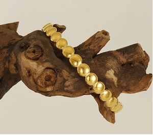 Polished gold beaded bracelet elegantly draped over natural wood in soft lighting