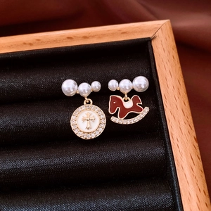 Macro detail of asymmetric pearl earrings with cross and red rocking horse pendants