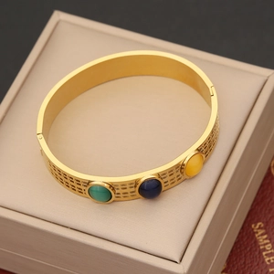 Detailed view of gold bangle with three colorful gemstones in a beige jewelry box