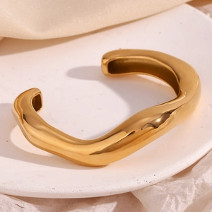 Detailed close-up of a high-polish gold irregular wavy cuff bangle on a white tray