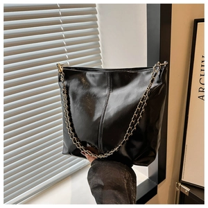 Detail of a soft black leather bucket bag with a gold metal chain strap and center stitching