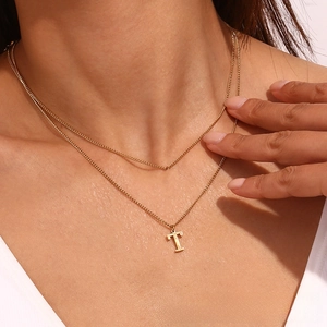 Detail of 18k gold layered necklace featuring a bold letter T pendant on the collarbone