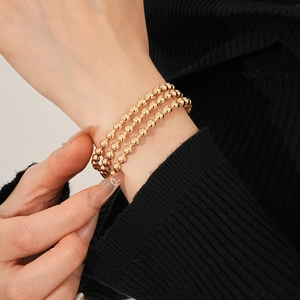 Dettaglio di un bracciale a tre strati di perline dorate indossato sul polso di una modella
