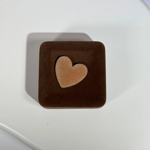 Top view of a square velvet jewelry box with a brown heart-shaped ornament on top