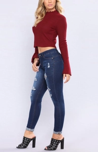 Détail du jean slim déchiré bleu foncé avec haut court en tricot bordeaux et mules