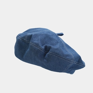 Detailed close-up of dark blue denim beret showing white contrast stitching and texture
