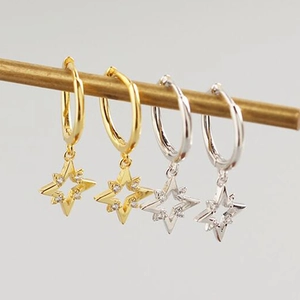Close-up of star-shaped hollow earrings with inlaid zircons in gold and silver finishes
