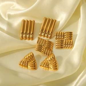 Detailaufnahme goldener geometrischer Ohrringe mit Webtextur auf champagnerfarbenem Satin