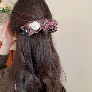 Détail d'une pince à cheveux à carreaux marron avec ours en peluche et nœud rouge