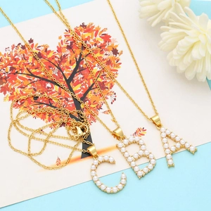 Close-up of gold alphabet A B C necklaces with faux pearl inlay and gold chain detailing