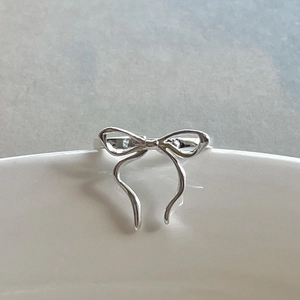 Minimalist 925 sterling silver bow knot open ring on white ceramic vessel edge
