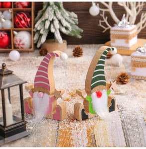 Close-up of pink and green wooden Christmas gnomes on snowy wood with festive decor