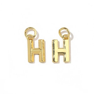 Detail of two 18K gold plated letter H charms with jump rings on a white background