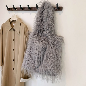 Detail view of a grey faux fur tote bag with long tassels hanging on a wooden wall hook