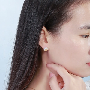 Dettaglio dell'orecchino con perla e base dorata indossato su modella stile sobrio