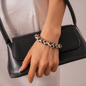 Detail shot of leopard print acrylic round bangle paired with a black leather bag