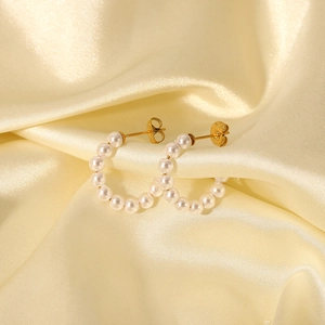 Detailed close-up of C-shaped hoop earrings with elegant pearls on gold silk fabric