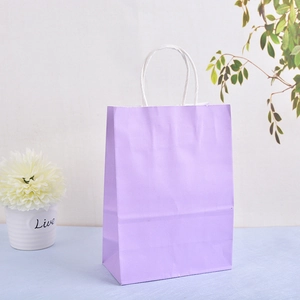Close-up of a lilac kraft paper gift bag with white twisted handles on a blue desk