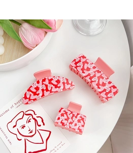 Three pink heart claw clips in rectangular and curved shapes on a clean white desk