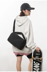 Detail of a black nylon cylinder crossbody bag worn by a model in casual street style