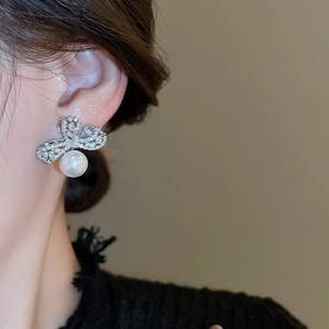 Close-up of silver bow earrings with zircon pavé and hanging white pearl on a model
