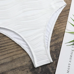Close-up of white swimwear with textured wavy fabric detail on a minimalist wood surface
