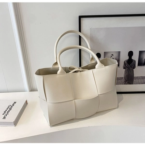 Detailed close-up of cream woven PU leather tote bag on minimalist studio background