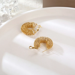 Macro shot of gold vintage hollow spring hoop earrings on a minimalist white tray