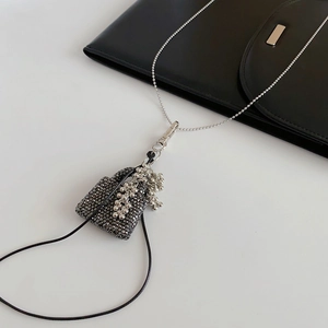 Détail d'un pendentif en forme de sac avec des strass noirs et des pompons argentés