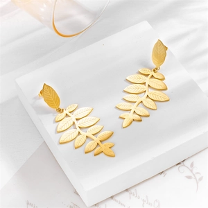 Elegant gold leaf dangle earrings displayed on a white marble stand for a luxury look