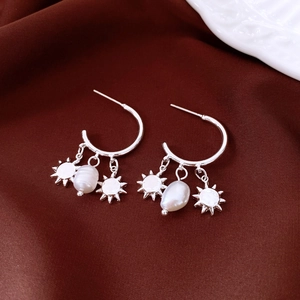 Detail of silver C-shape earrings with baroque pearl and sun charms on dark cloth