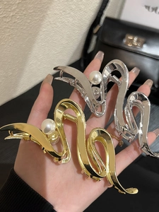 Detail of S-shaped gold and silver metal hair claws with large pearl accents for women