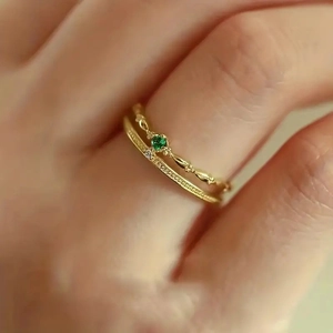 Détail de bagues superposées en or avec zircon vert et texture perlée sur le doigt