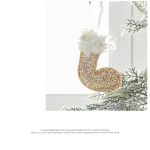 Close-up of golden glitter Christmas stocking ornament hanging on snow-covered pine branch