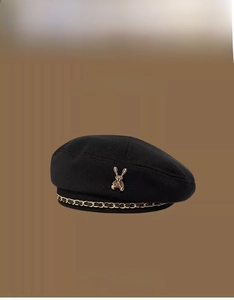 Detail of black beret featuring a 3D gold rabbit emblem and black gold woven chain accent