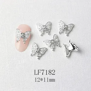 Macro detail of silver butterfly nail charms with pearls and rhinestones on a pink nail
