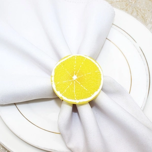 Detail of yellow lemon slice napkin ring on white napkin and ceramic plates