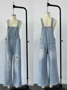 Detailed close-up showing distressed ripped denim fabric and raw hem on blue overalls