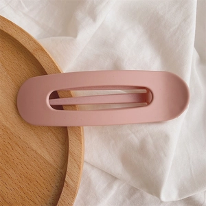 Close-up of a matte pink hollow oval duckbill hair clip on a wooden tray background
