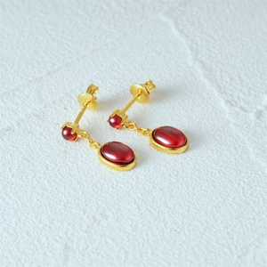 Detail of vintage gold earrings featuring oval red gemstones on a white textured background
