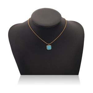 Close-up of golden necklace with a blue square enamel pendant on a black mannequin