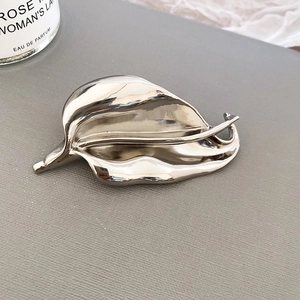 Polished silver leaf brooch with minimalist design on textured background