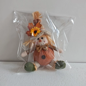 Detail of harvest scarecrow doll with maple leaf and sunflower in clear packaging