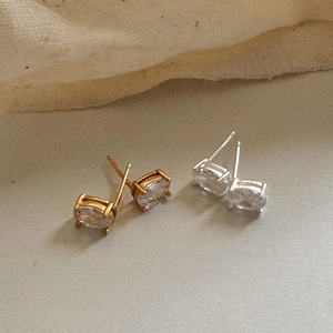Detailed view of silver and gold oval stud earrings with four-prong set zircons
