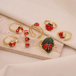 Macro shot of gold ladybug rings with red enamel and pearls on beige stone texture