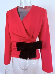 Detail of red long-sleeve wrap top featuring a large black velvet bow at the waistline