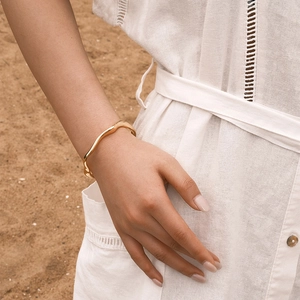 Elegante brazalete abierto dorado ondulado en la mano de modelo en entorno natural