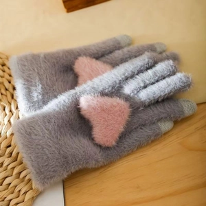 Close-up of gray plush knit gloves with pink heart applique on a rustic wooden background